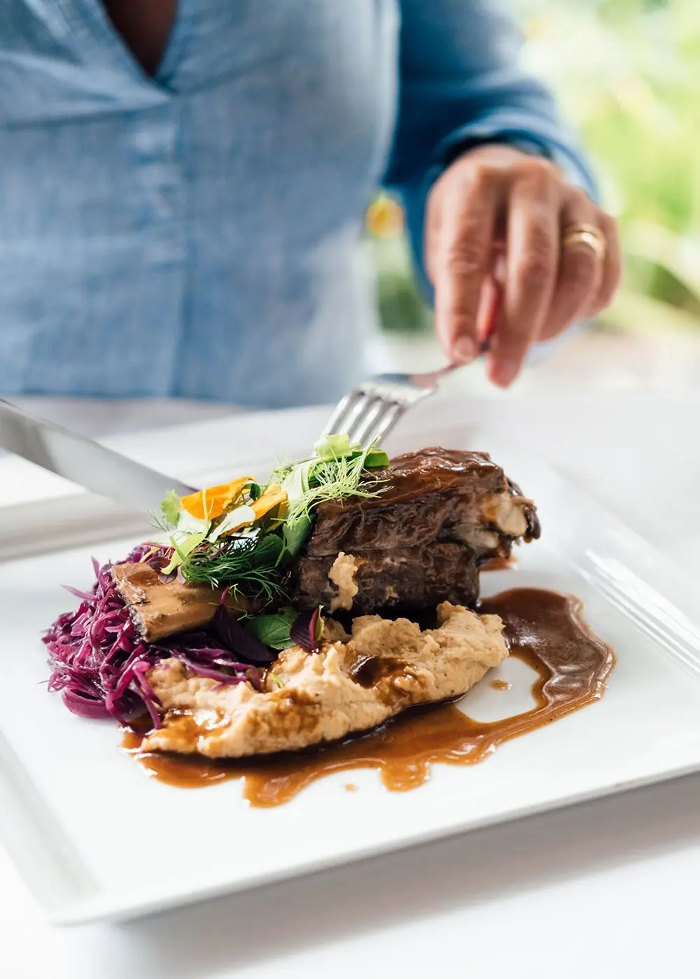 Guest cutting into a plated meat dinner with vegetables and sauce at Gibb's Farm