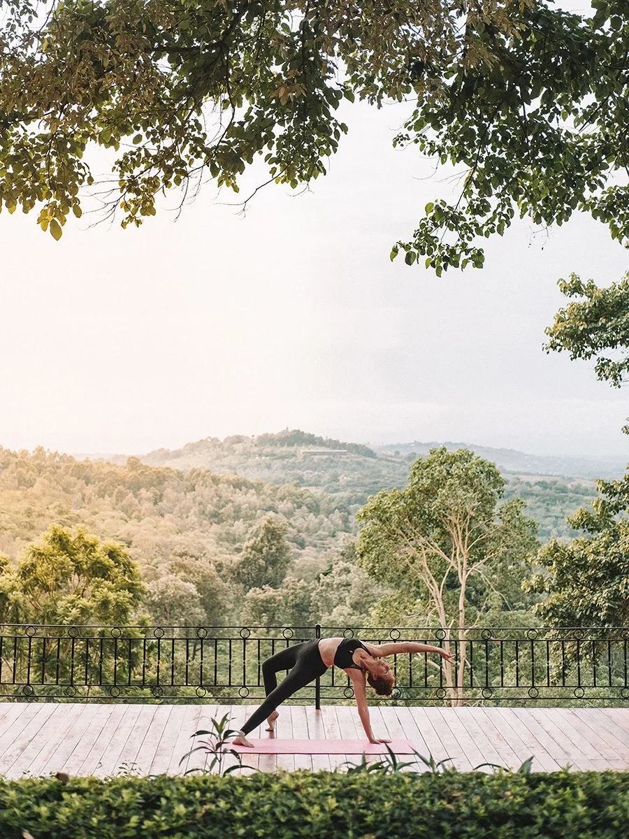 Woman doing a yoga pose on a wooden platform overlooking forested hills