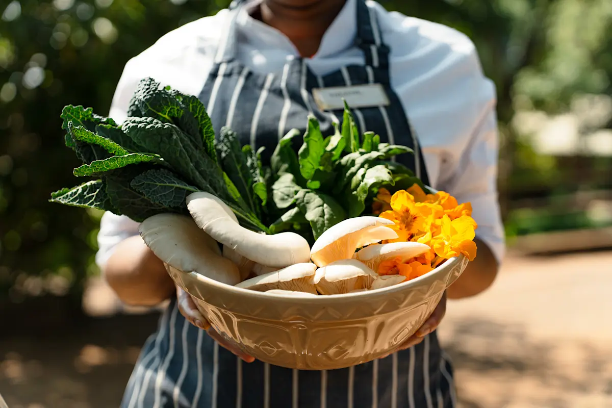 Chef holding a bowl of fresh greens, mushrooms and flowers from the Gibb's Farm garden