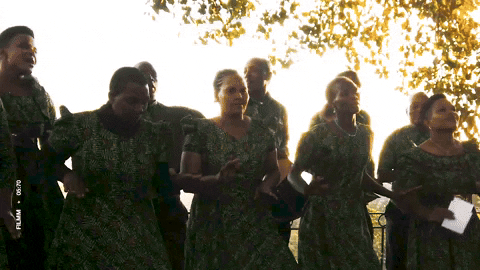 Choir in matching green dresses singing outdoors in golden light