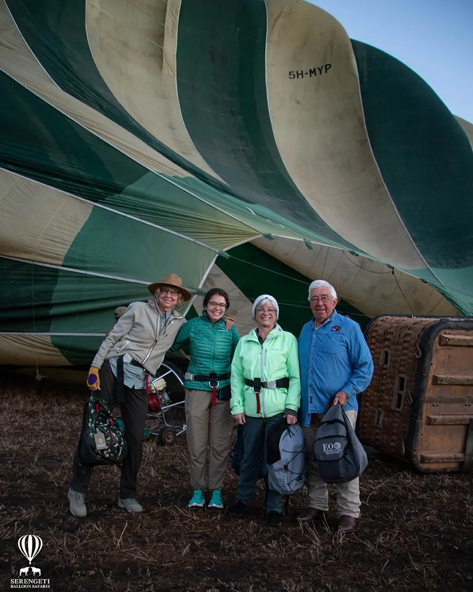 Four smiling guests standing in front of a deflating hot air balloon at dawn