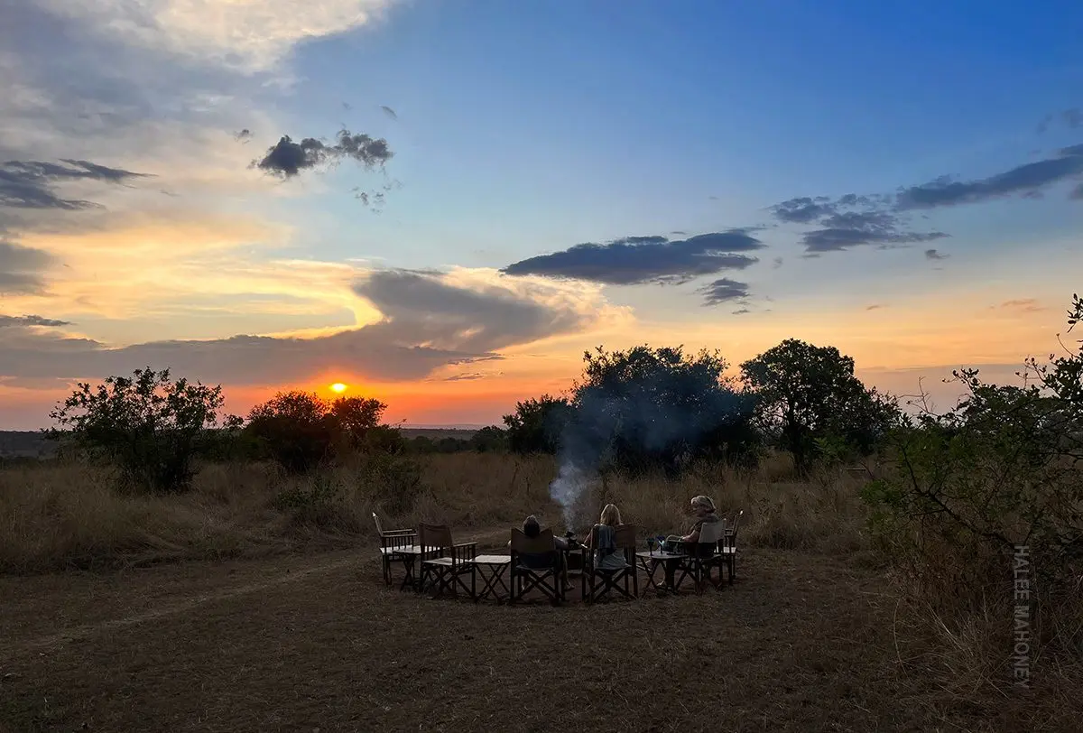 Guests sitting around a campfire on the plains as the sun sets