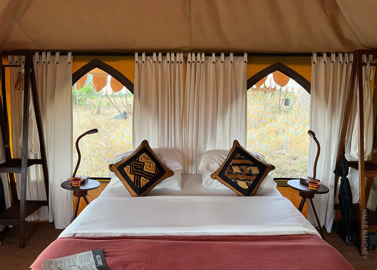 Safari tent bedroom with a made bed, patterned pillows and open windows onto the bush