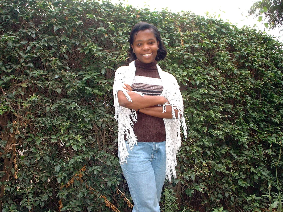 Rose Ngilisho early in her career, standing with arms crossed in front of a hedge