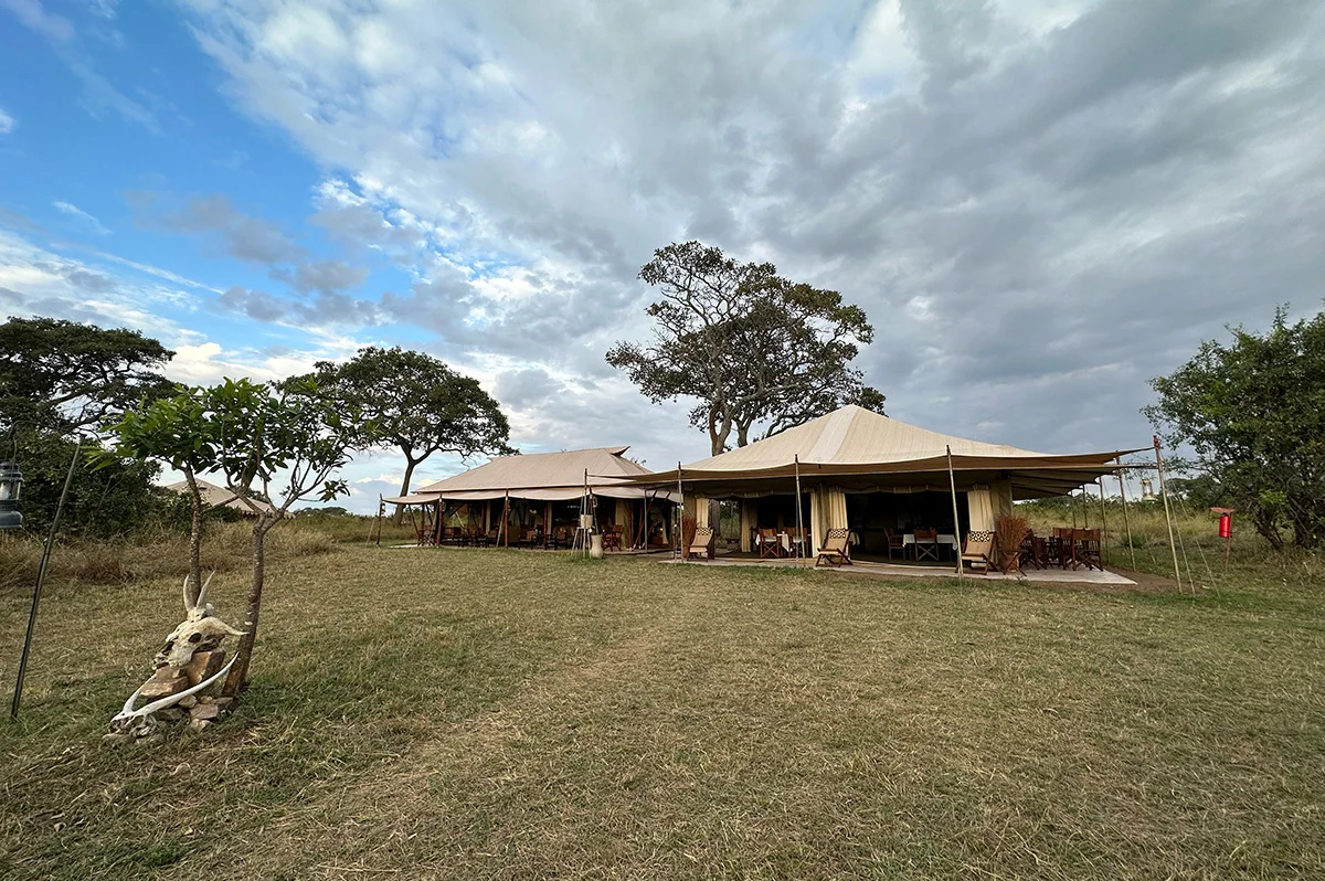 Large canvas mess tents of a safari camp on grassland under a cloudy sky