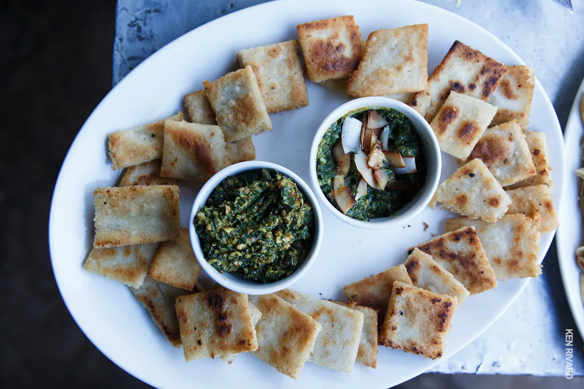 Platter of crispy flatbread squares around two bowls of green dip