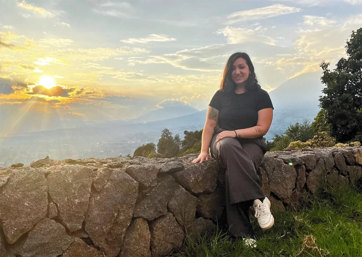 Portrait of Francesca Panzariello sitting on a stone wall above a valley at sunset