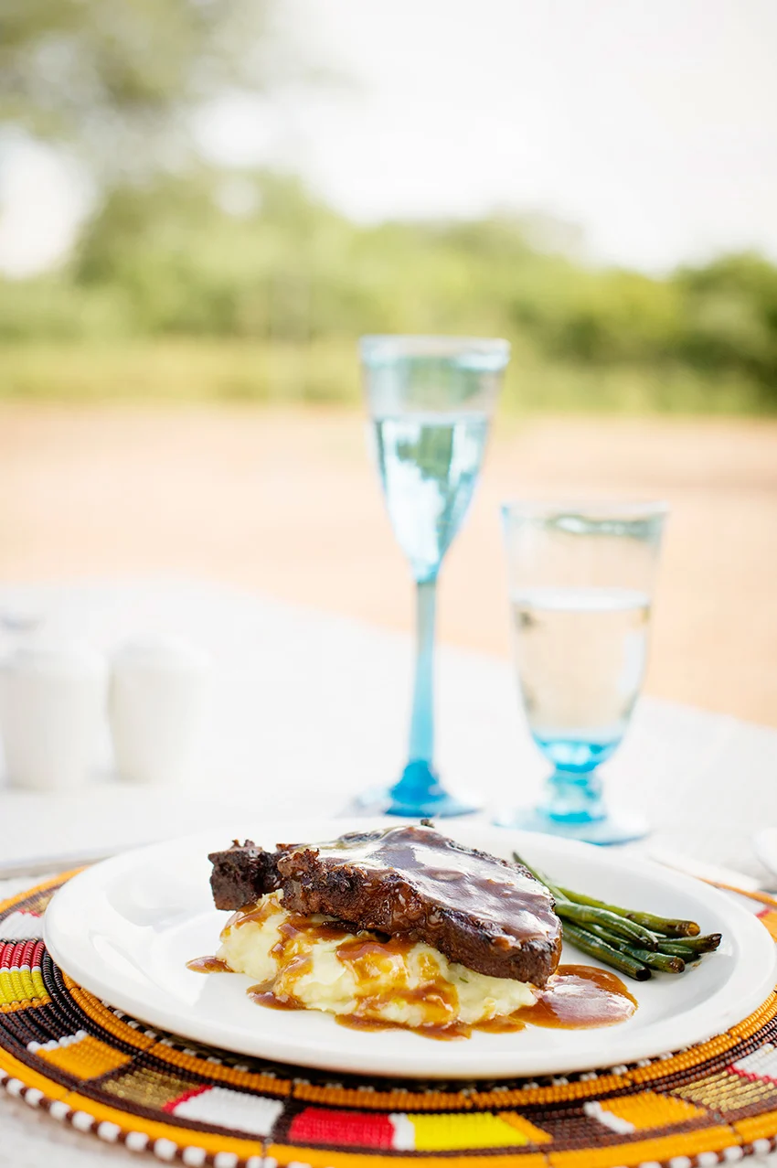 Plate of braised beef with gravy, mashed potatoes and green beans on a beaded placemat