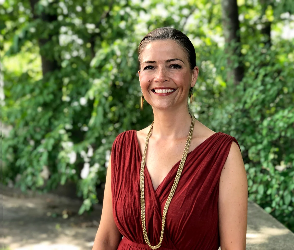 Portrait of Ina Steinhilber smiling outdoors in front of green foliage