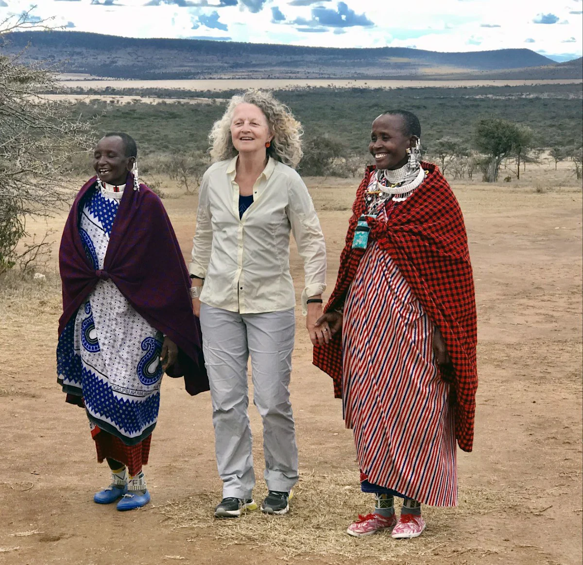Judi Wineland holding hands with two smiling Maasai women in traditional dress