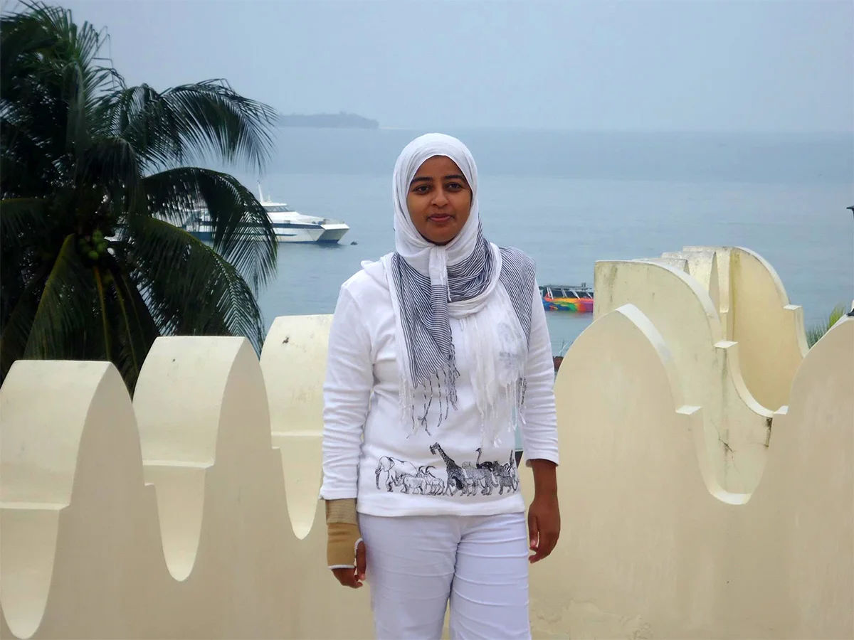 Portrait of Shamim Issa on a seaside rooftop terrace with boats in the harbor behind her