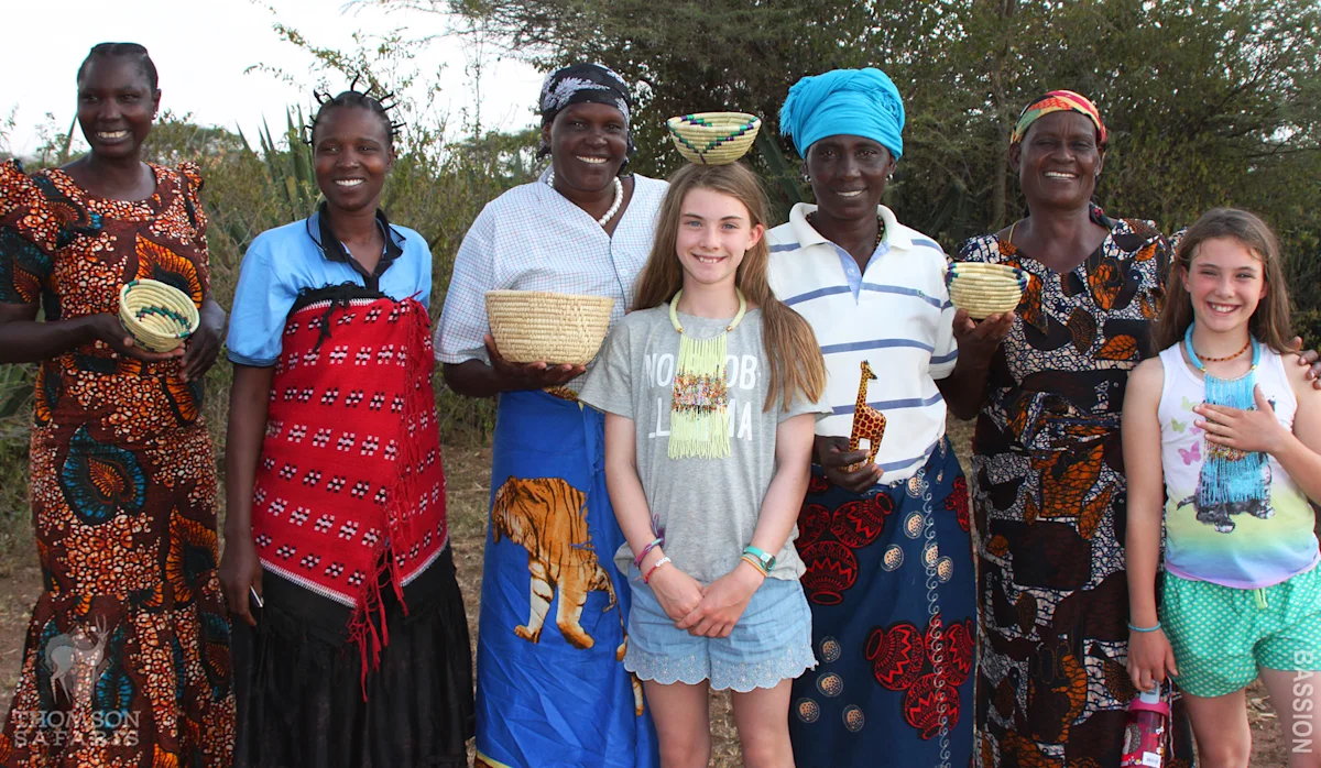 Two young girls posing with a group of smiling women holding woven baskets