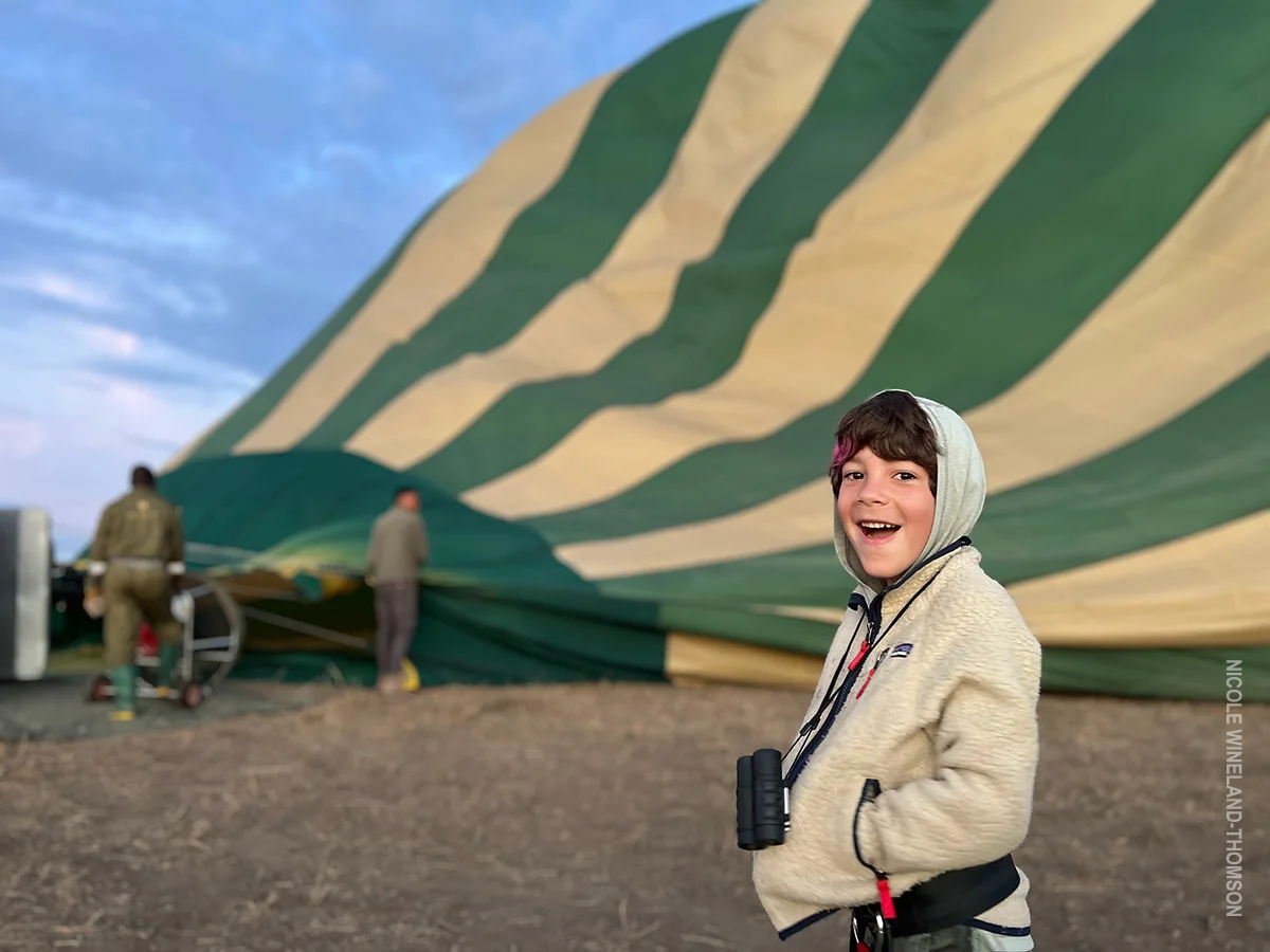 Excited child with binoculars in front of a green and cream hot air balloon being inflated