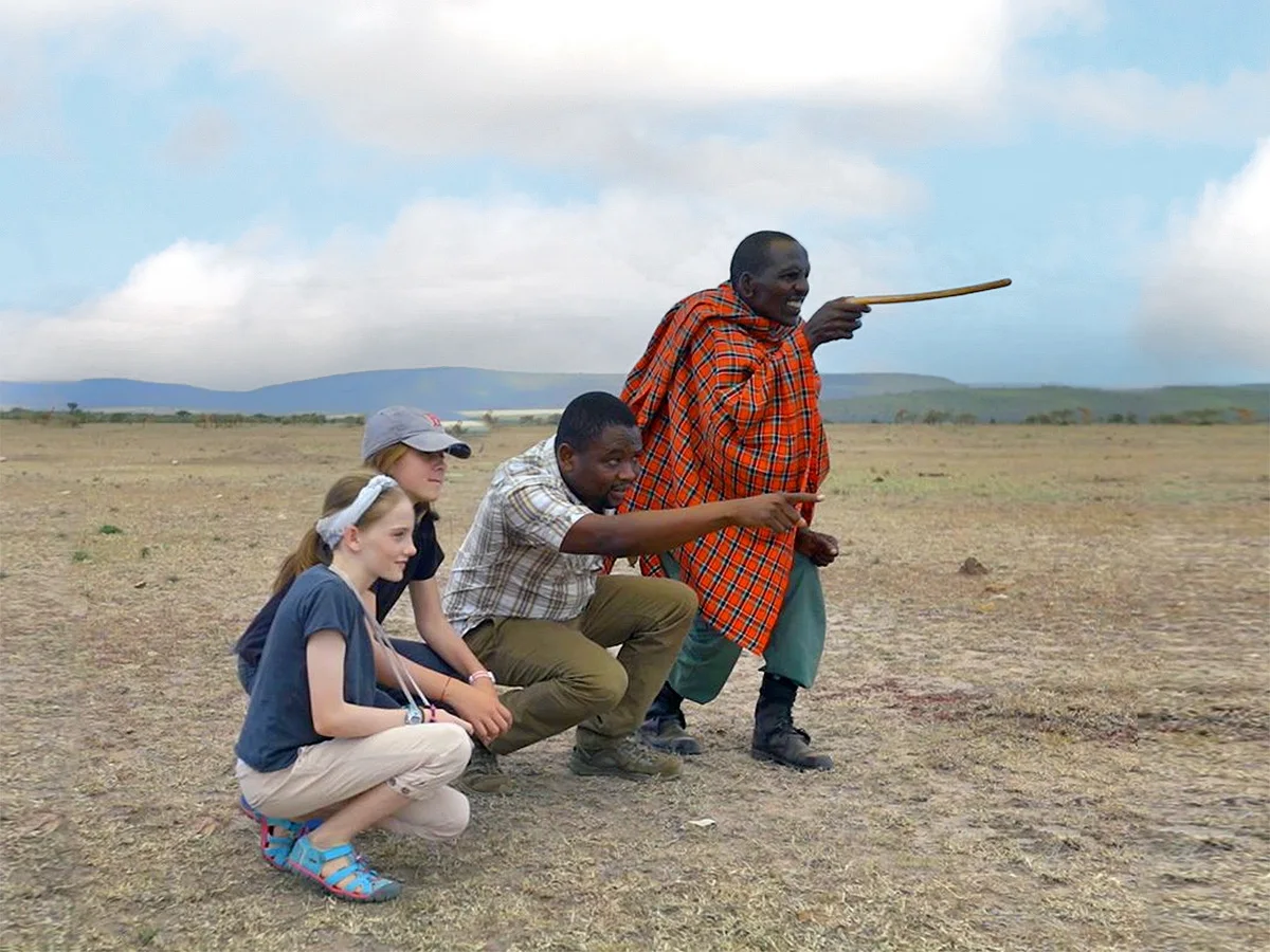 Guide and Maasai guide pointing across the plains as two girls crouch beside them