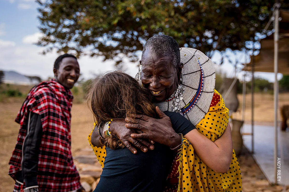 Maasai woman in a beaded collar warmly hugging a young traveler