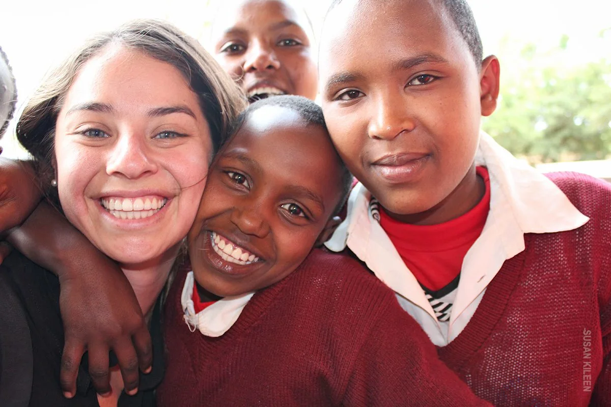 Smiling young traveler embracing schoolgirls in maroon sweaters