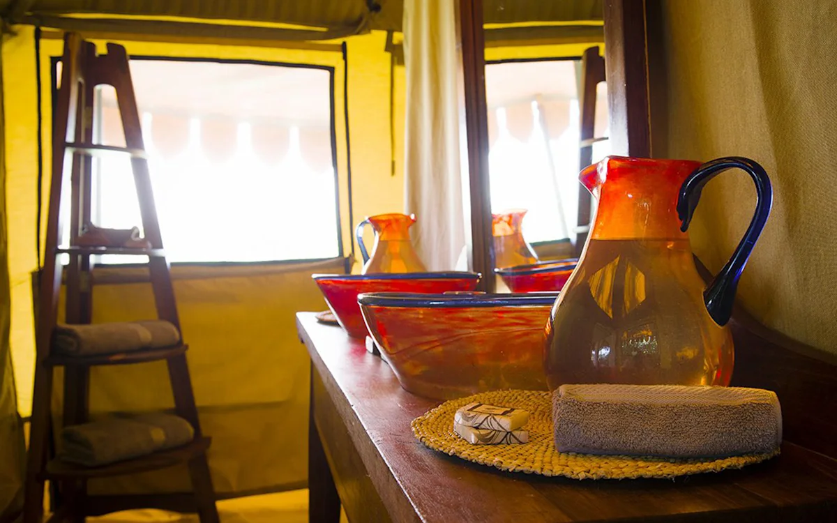 Orange glass pitcher and basins on a wooden vanity inside a tent at Tarangire Nyumba