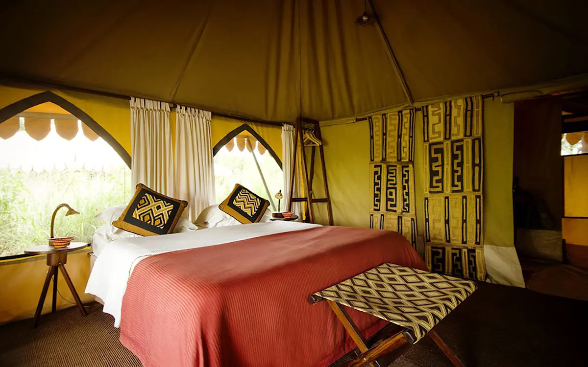 Double bed with red blanket and patterned pillows inside a tent at Tarangire Nyumba