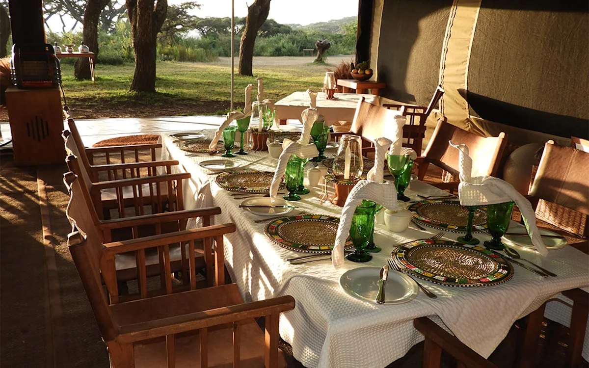 Long dining table set with green glasses and beaded placemats at Ngorongoro Nyumba