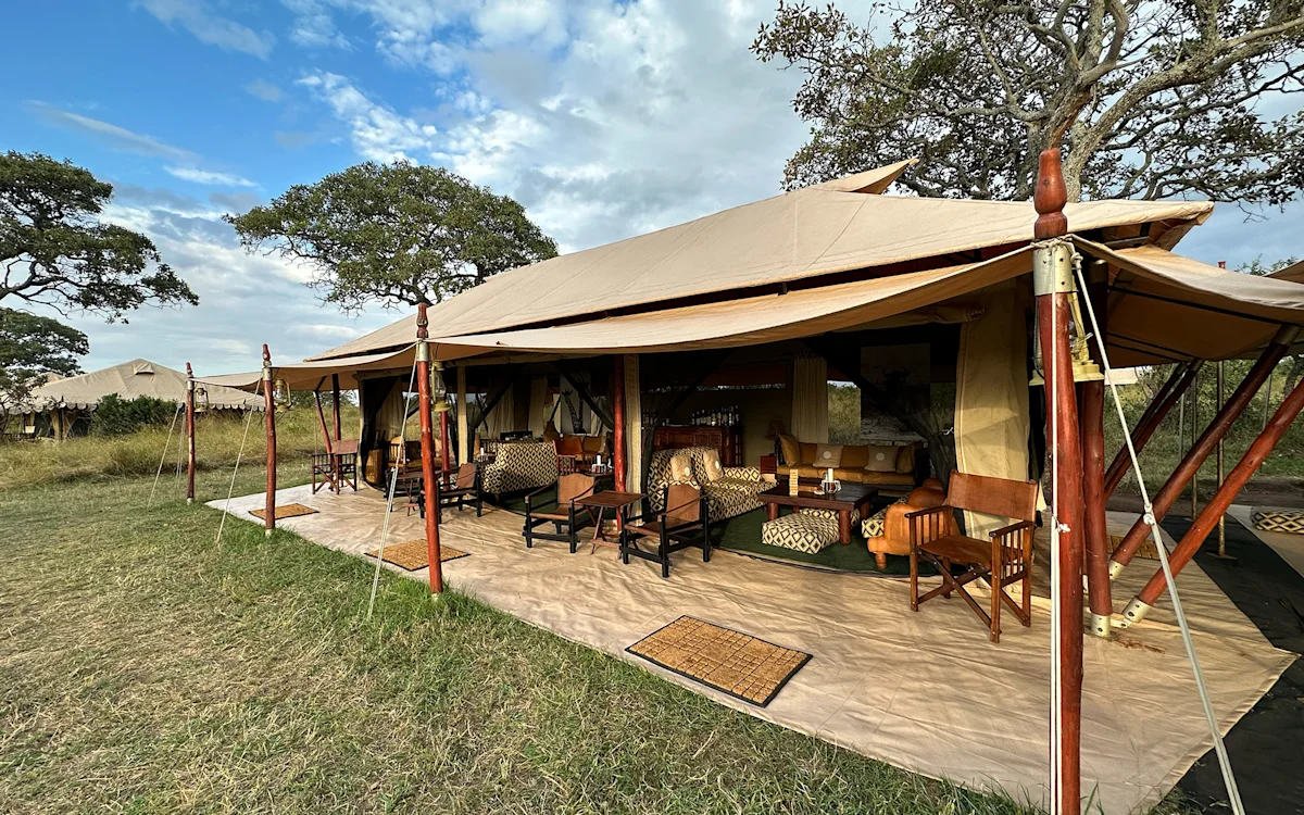 Open-sided lounge tent with armchairs on a grassy lawn at Serengeti Nyumbas