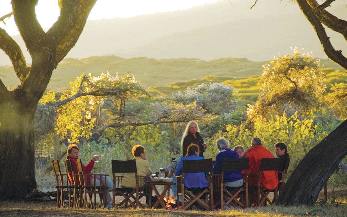 Travelers gathered around a campfire beneath trees at Ngorongoro Nyumba