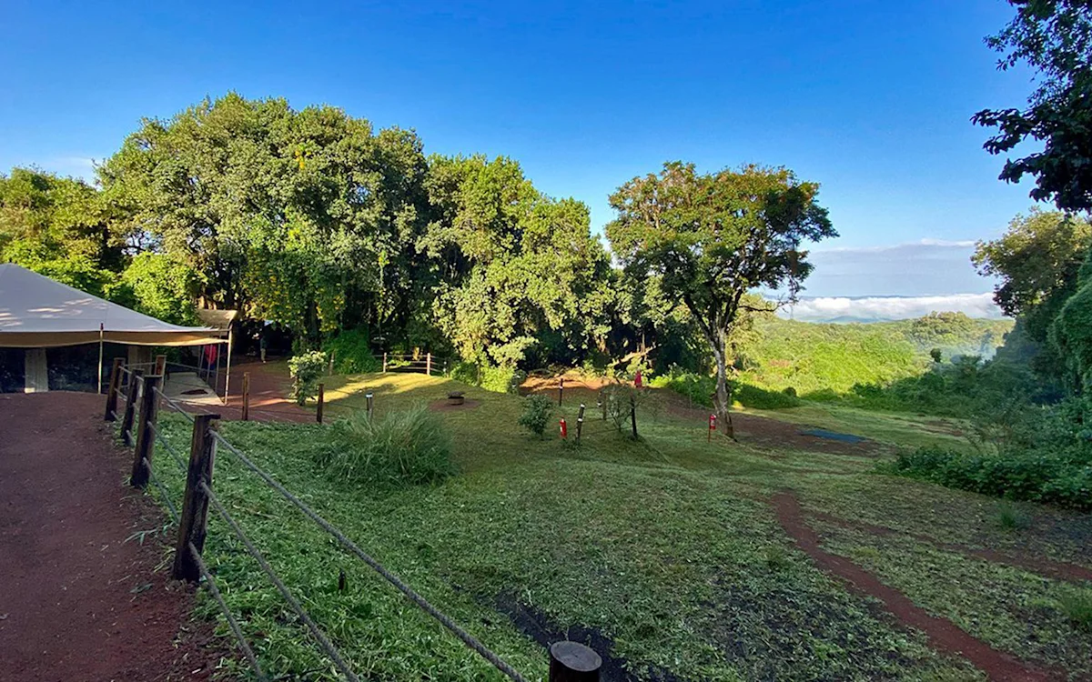 Grassy camp grounds and trees with a view to distant hills at Ngorongoro Nyumba