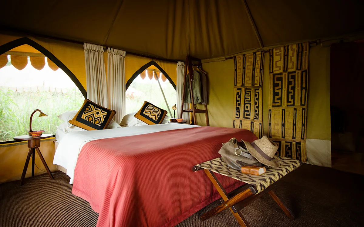 Double bed with red blanket and patterned pillows inside a tent at Eastern Serengeti Nyumba