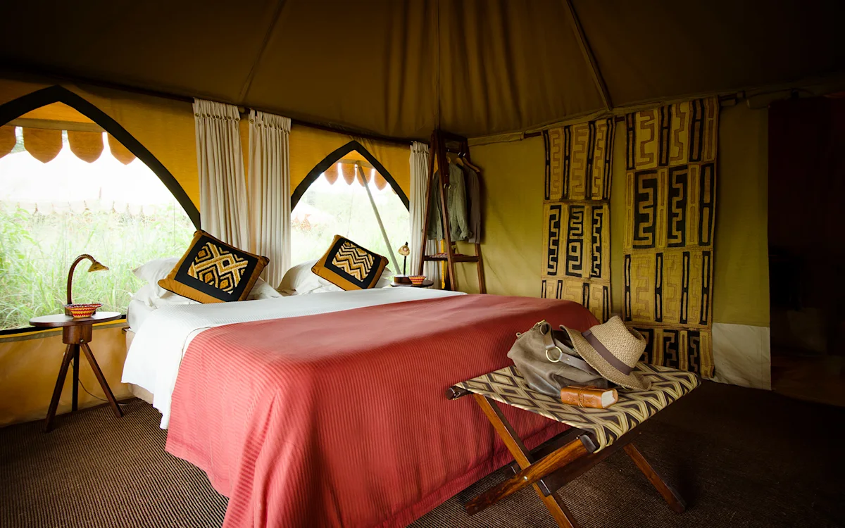 Double bed with red blanket and patterned pillows inside a tent at Serengeti Nyumbas