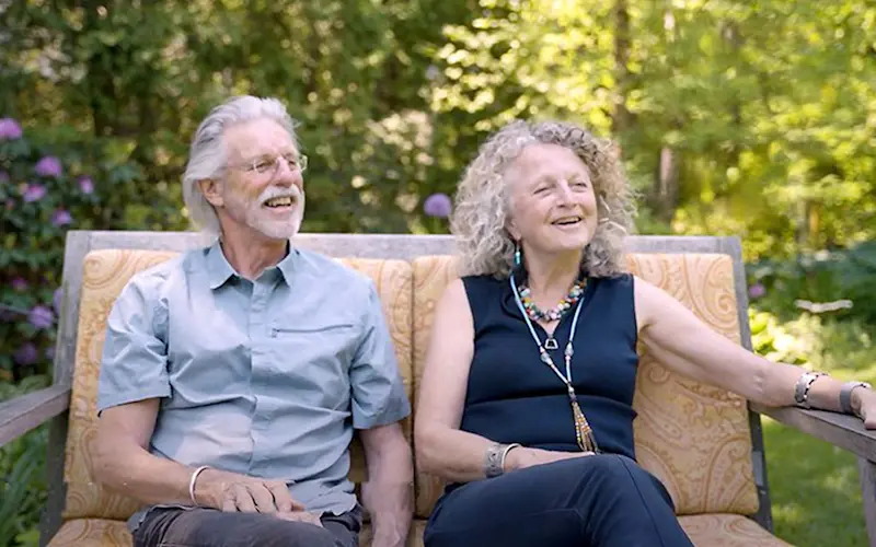 Rick Thomson and Judi Wineland laughing together on a garden bench