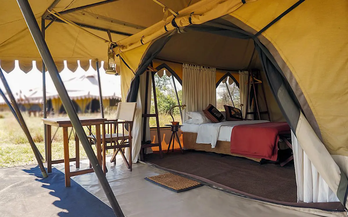 Open tent porch looking into a bedroom with a double bed at Serengeti Nyumbas
