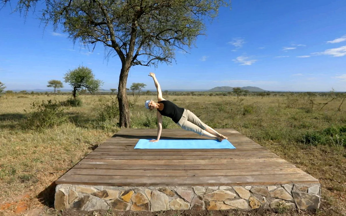 Guest holding a side plank on a yoga platform on the open plains at Serengeti Nyumbas
