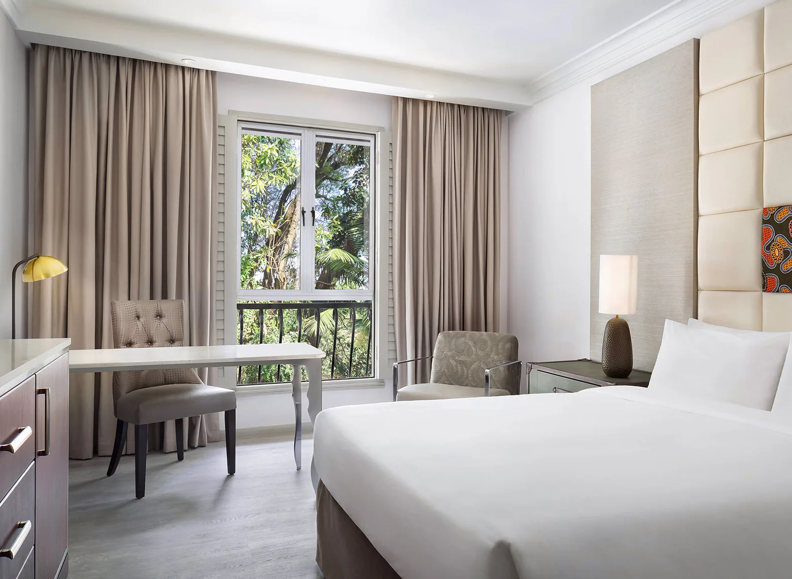 Bright guest room with a double bed, desk and balcony at The Arusha Hotel