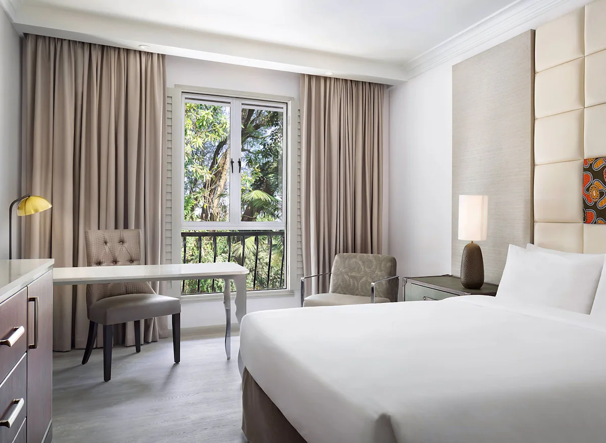 Bright guest room with a double bed, desk and balcony at The Arusha Hotel