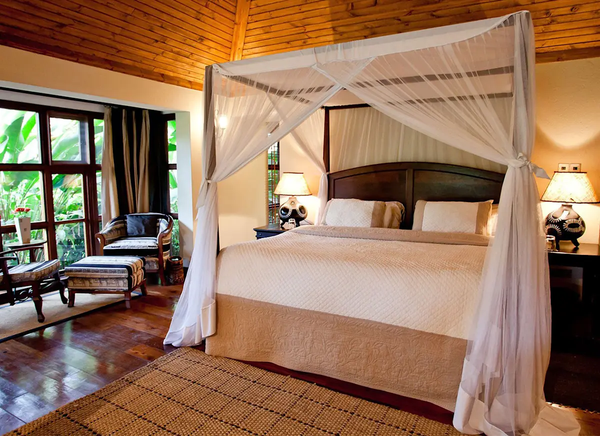 Four-poster bed with mosquito net in a wood-paneled room at Legendary Lodge