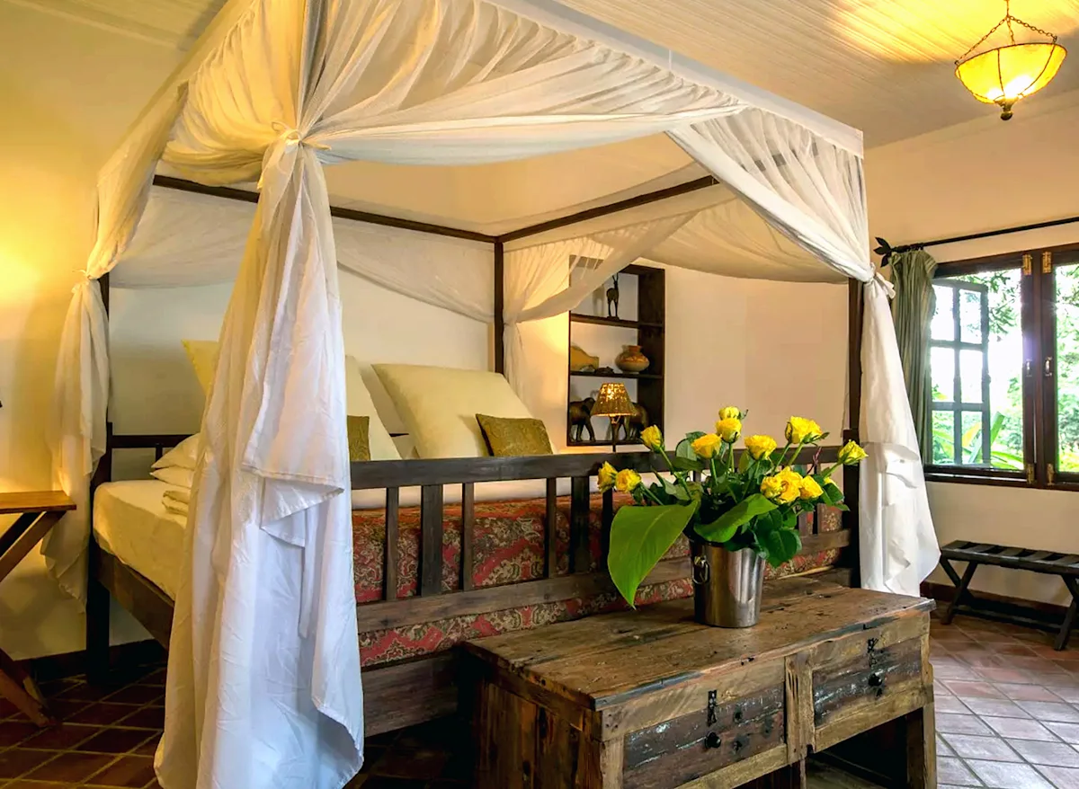 Four-poster bed with mosquito net and yellow flowers at Rivertrees Country Inn
