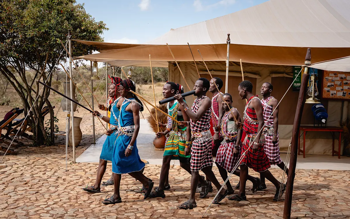 Maasai men and women in colorful dress dancing in front of a safari tent