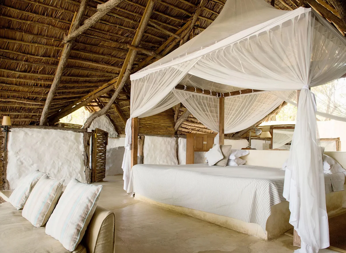 Guest room with a canopied bed under a thatched roof at Sand River Selous