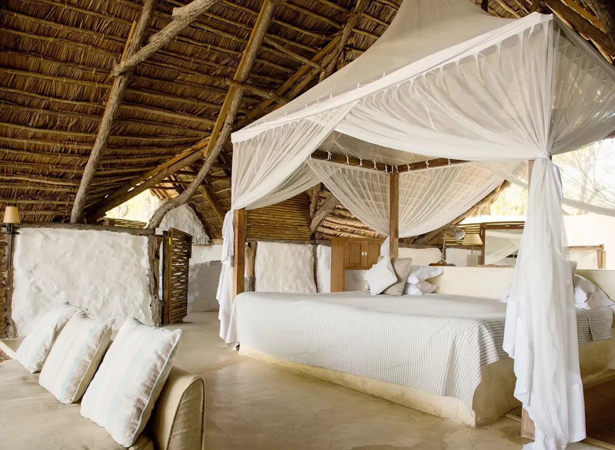 Guest room with a canopied bed under a thatched roof at Sand River Selous