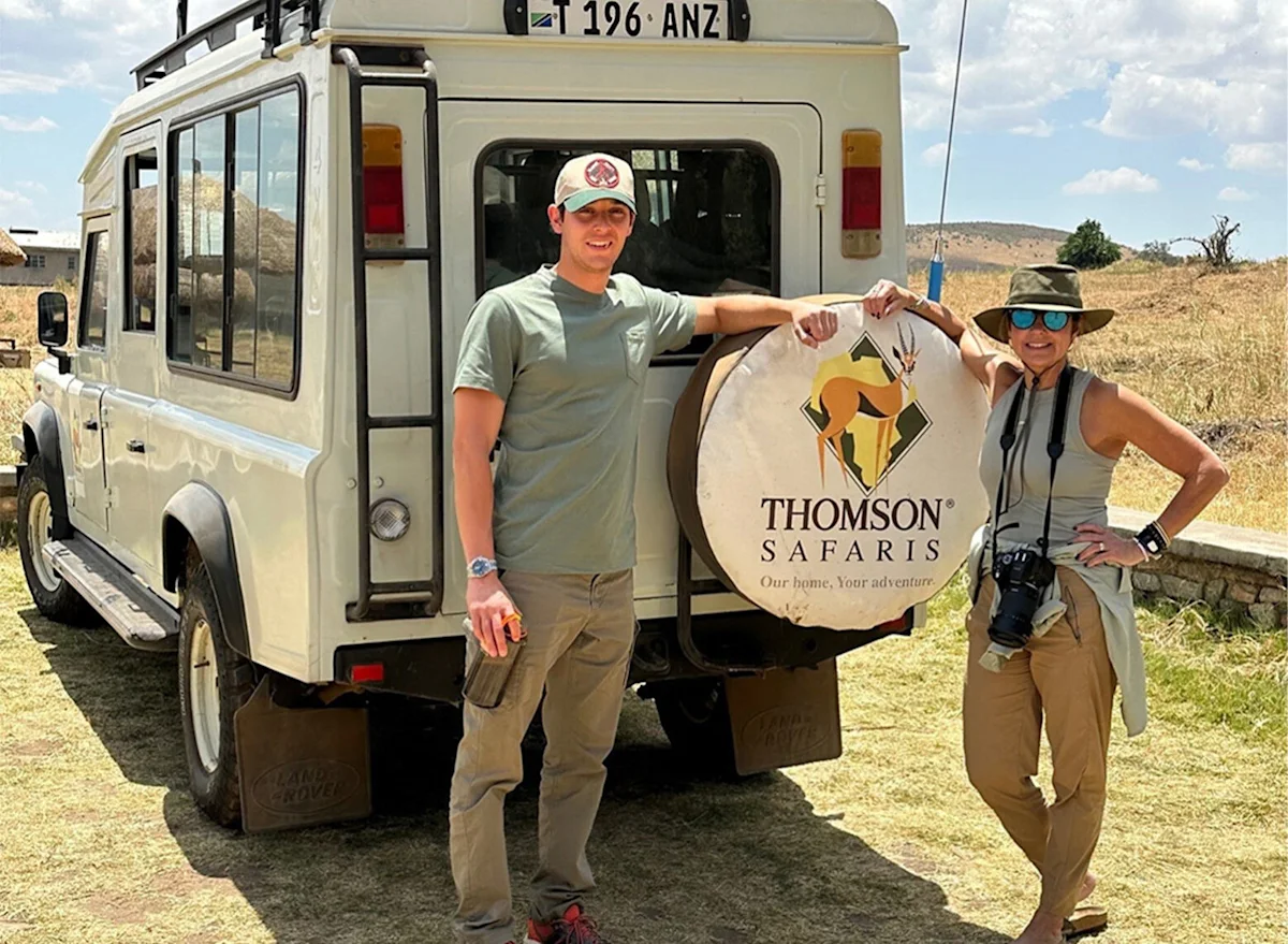 Two travelers posing beside a Thomson Safaris vehicle