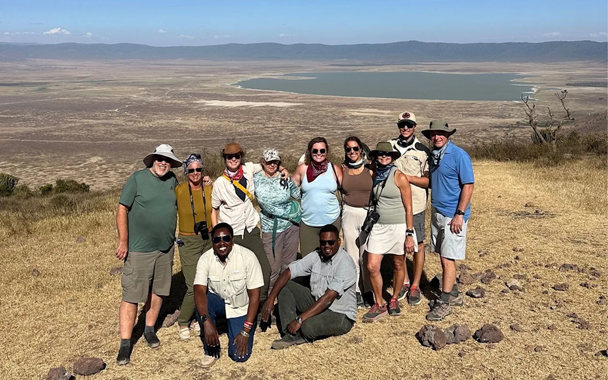 Group of travelers and two guides posing on a crater rim overlooking a lake on the crater floor