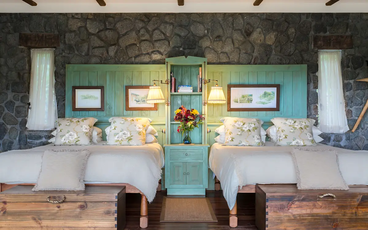 Twin beds against a stone wall with a turquoise headboard at Gibb's Farm
