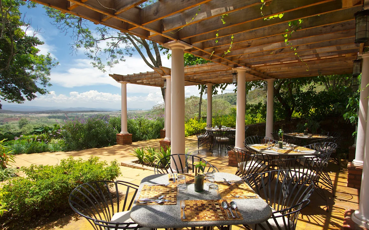 Outdoor restaurant terrace under a pergola with a valley view at Gibb's Farm