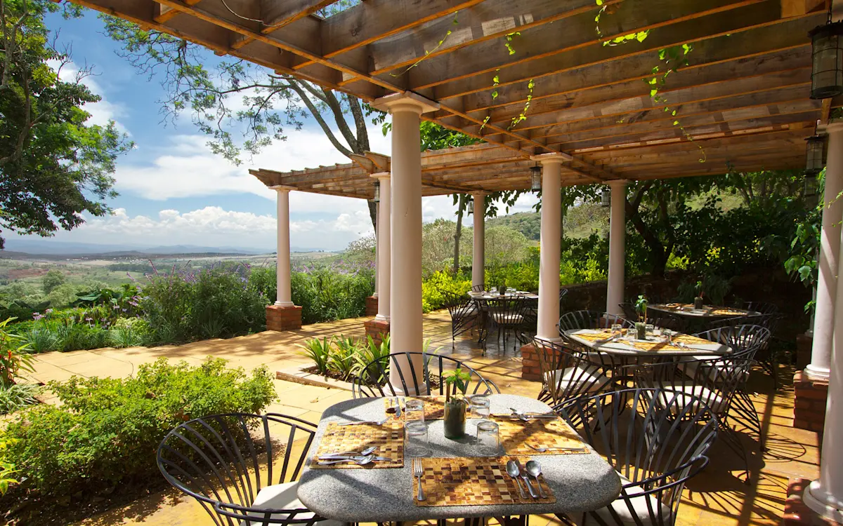 Outdoor restaurant terrace under a pergola with a valley view at Gibb's Farm