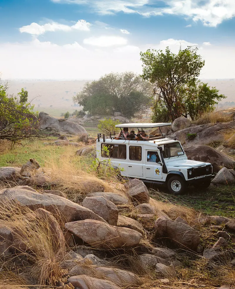 Safari vehicle with photographers parked among rocks and grass on the savanna
