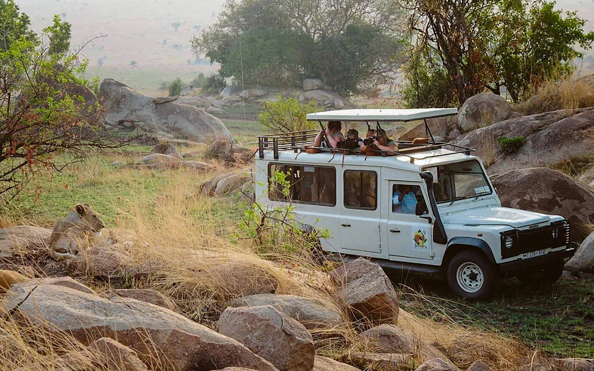 Travelers in an open-roof safari vehicle parked among boulders