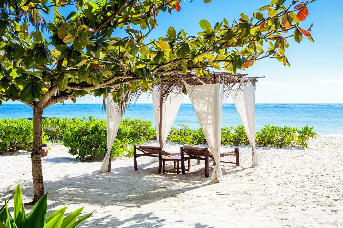 Curtained cabana with two lounge chairs on a white sand beach in Zanzibar