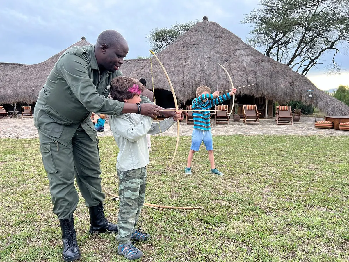 Guide teaching children to shoot a bow and arrow on a camp lawn