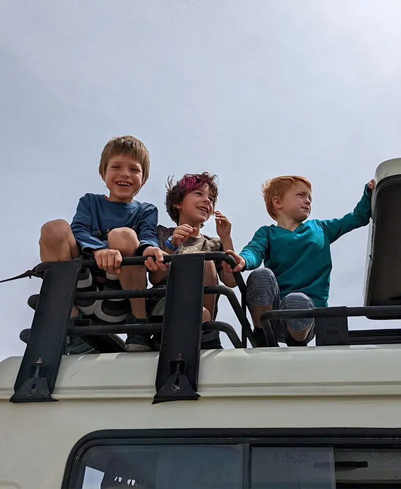Three smiling boys sitting on the roof of a safari vehicle