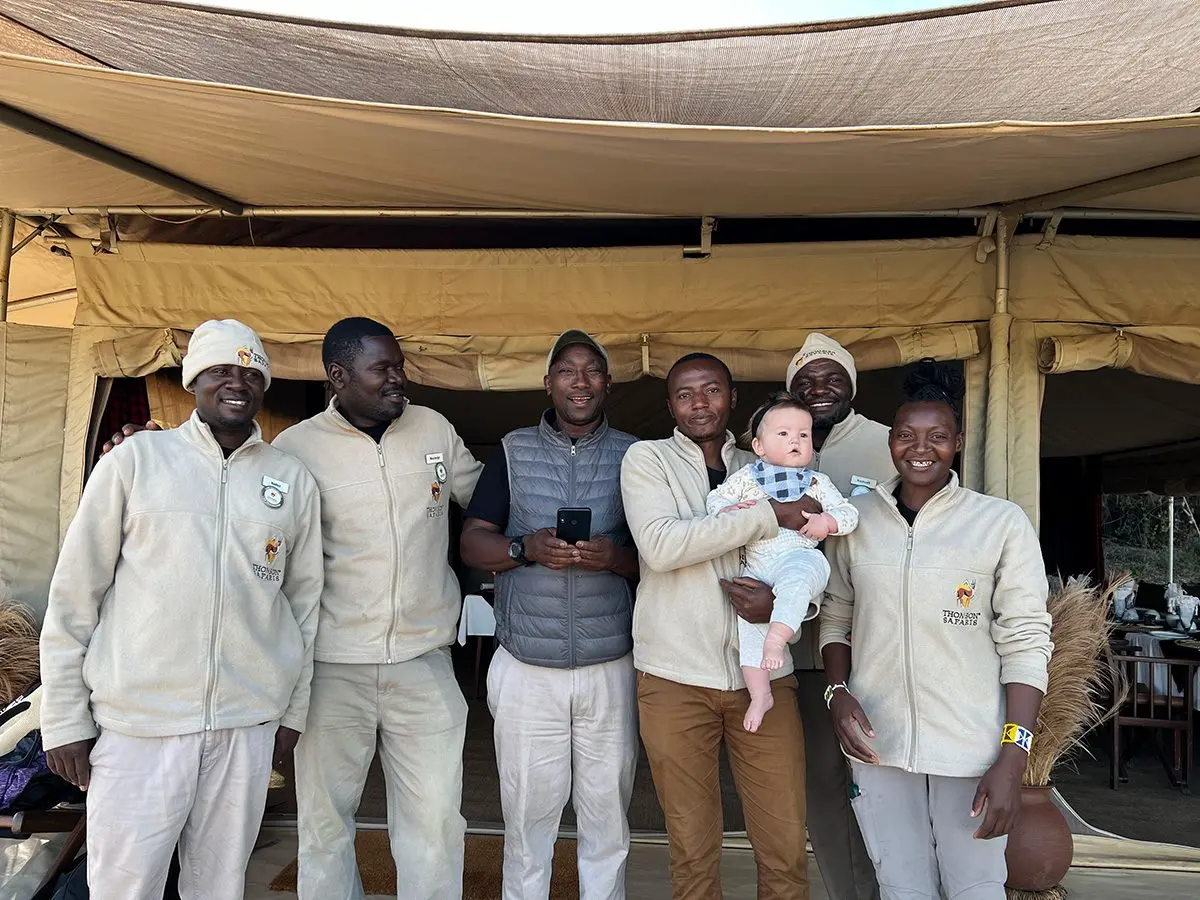 Thomson camp staff posing in front of a tent, one holding a baby