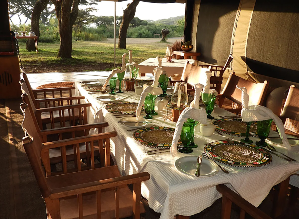 Long dining table set with green glasses and beaded placemats at a Nyumba camp